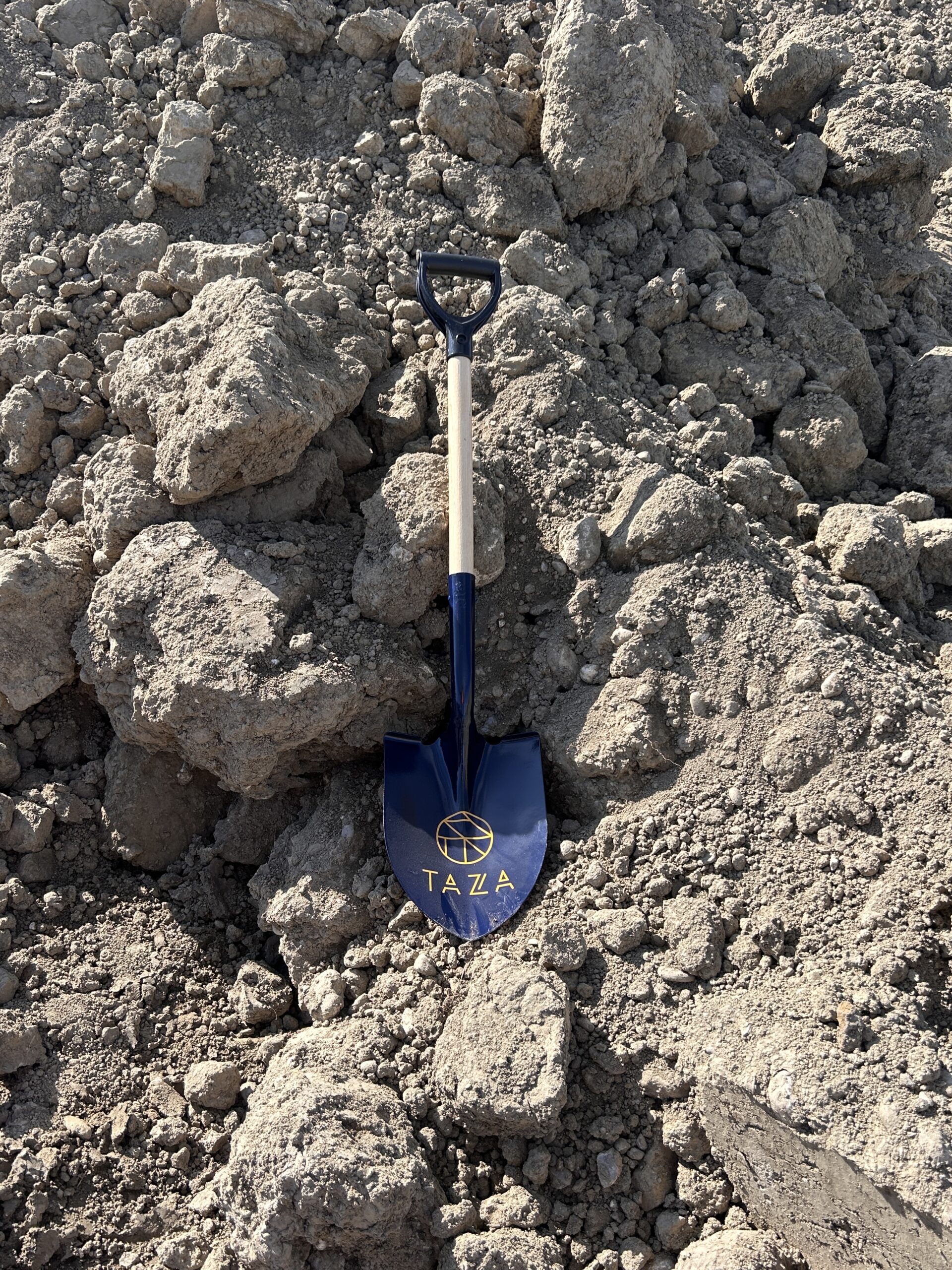 Blue shovel with Taza logo resting in dirt