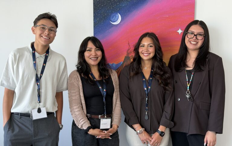 Four people in office attire standing in front of a brightly coloured painting