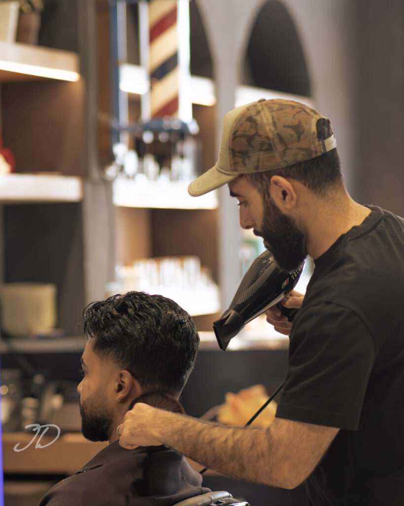 Barber wearing a ball cap blowdrying the back of a man's hair