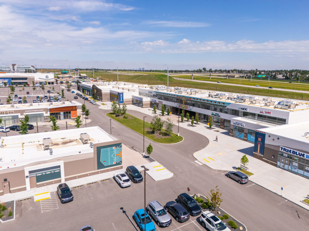 Aerial view of The Shops at Buffalo Run featuring blue skies, green grass, and cars parked at different storefronts below.