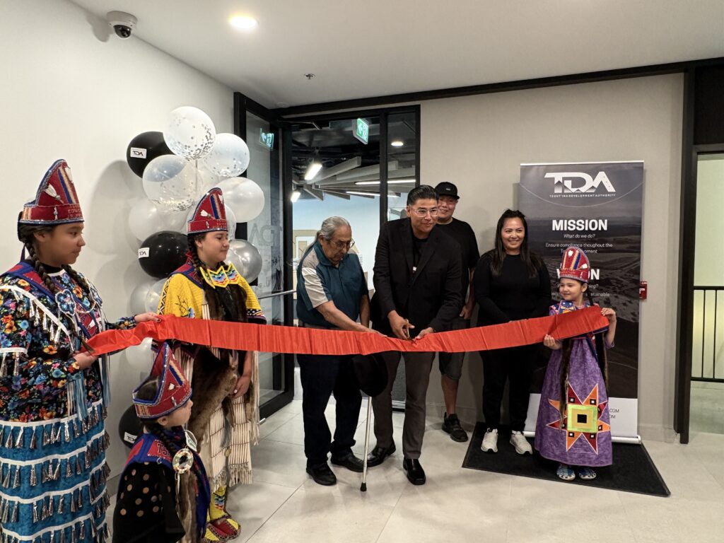 TDA team members and youths dressed in traditional Tsuut'ina Nation regalia cut a red ribbon in front of the TDA office door.
