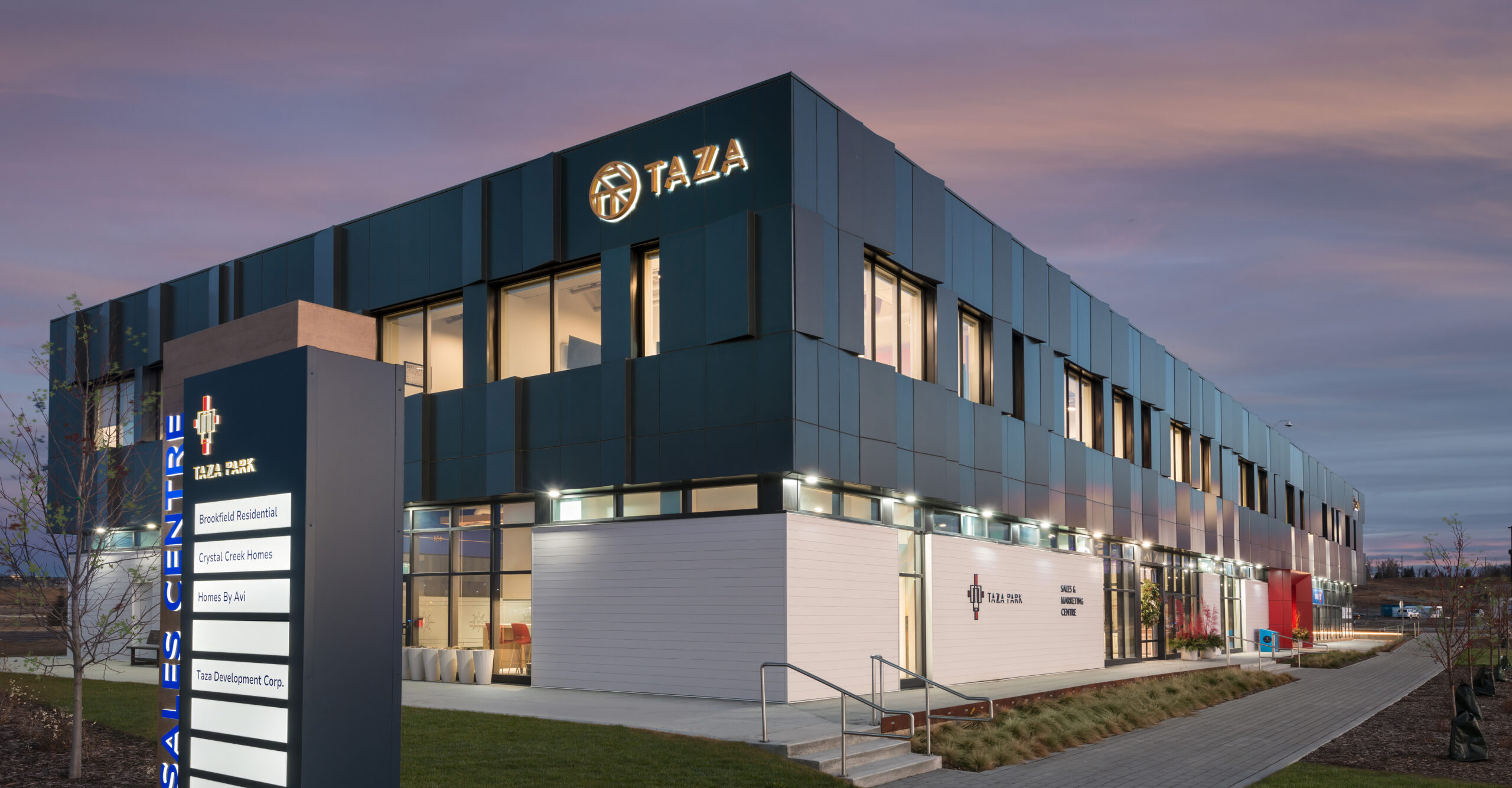 Taza Park Sales & Marketing Centre exterior with green grass and sunset background.