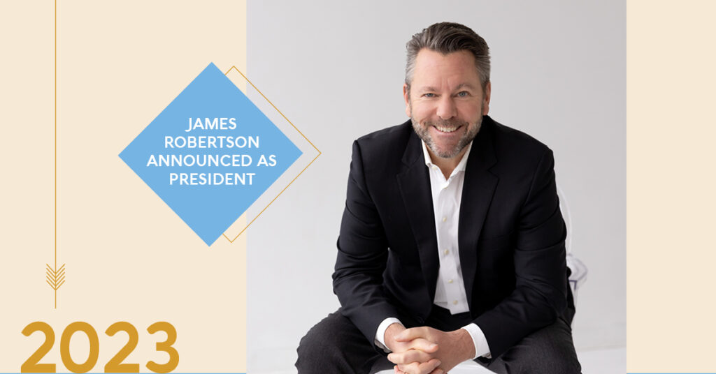 Taza President James Robertson wearing a black suit and white shirt, sitting down and smiling.