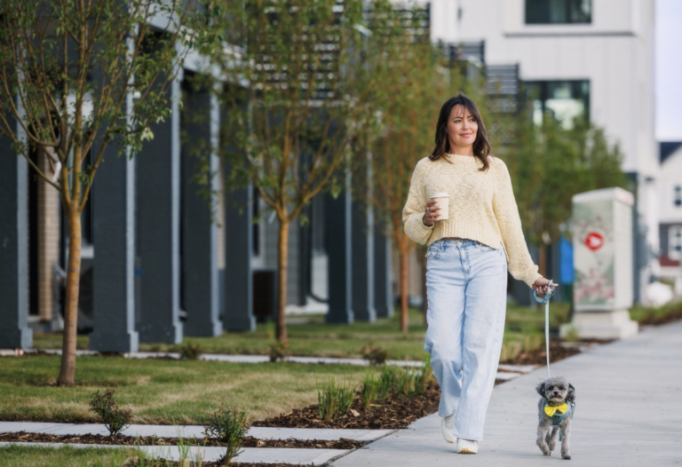 Woman walking a small dog on the sidewalk next to a row of townhomes.