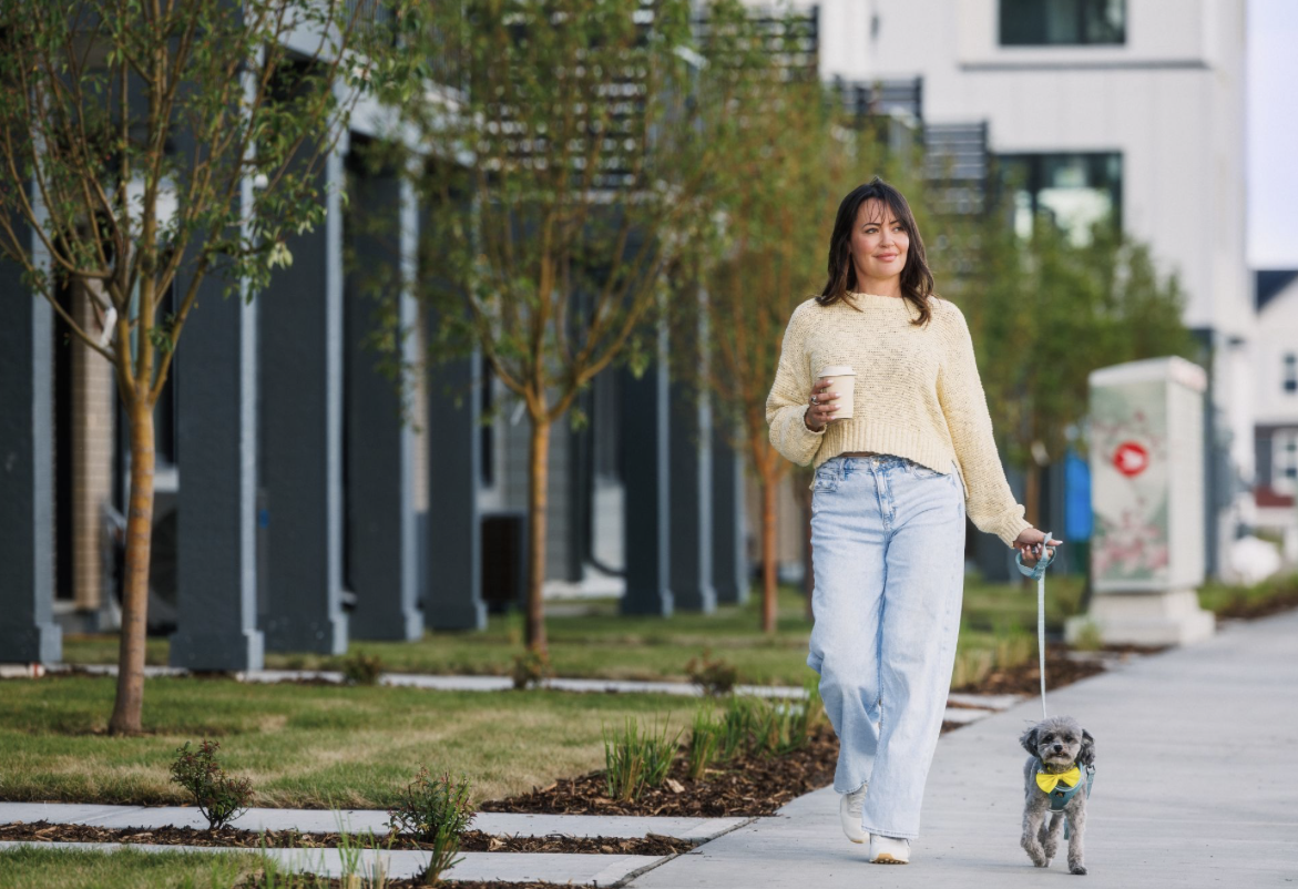Woman walking a small dog on the sidewalk next to a row of townhomes.
