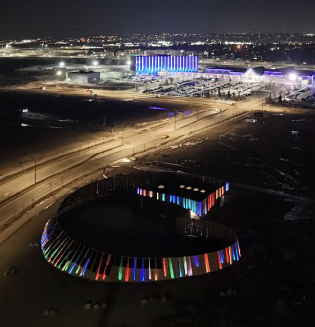 Nighttime aerial view of the Taza Park water reservoir with multi-coloured lights bordering the exterior of the building.