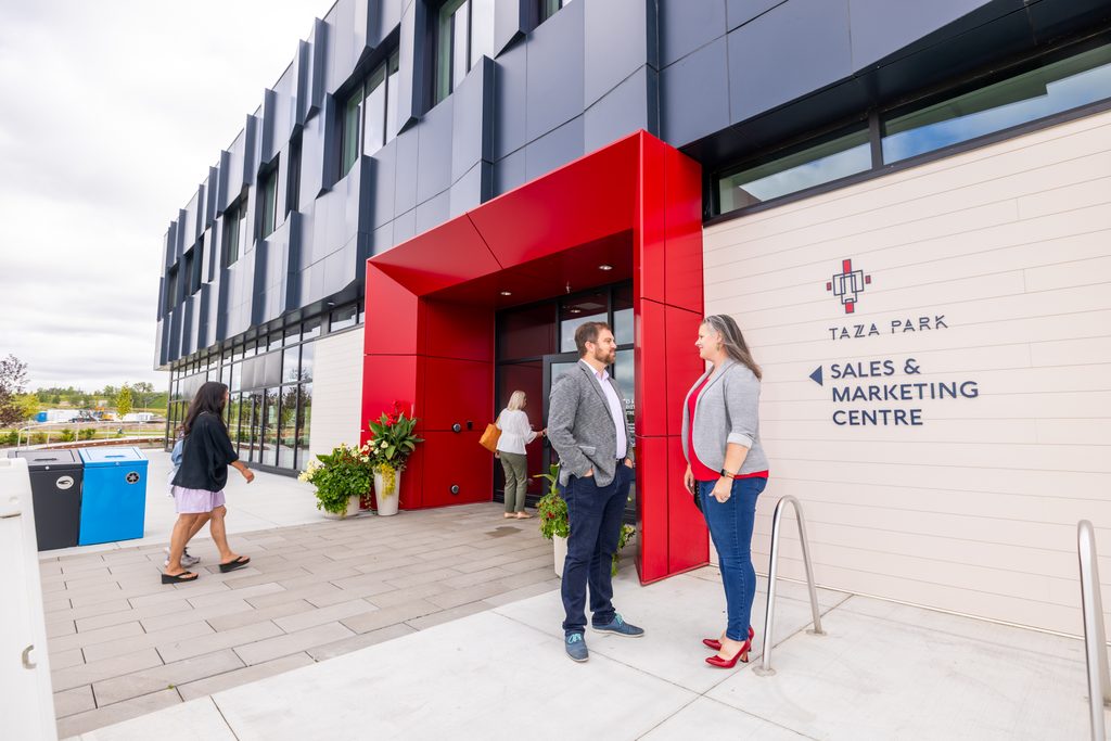Visitors outside the Taza Park Sales & Marketing Centre, with its striking red entrance canopy and angular navy facade.