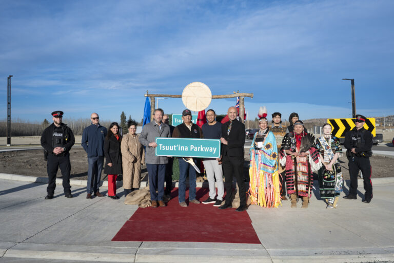 Group of people holding a green street sign for "Tsuut'ina Parkway" on a red carpet in front of a decorative wood arch.